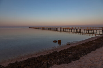 Fototapeta premium Long pier near the sea. Beautiful summer evening. Smooth water with reflection.