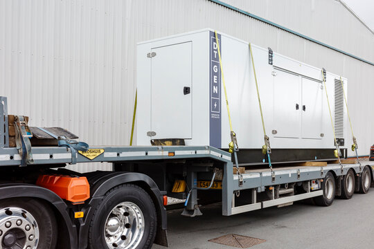 Heavy-duty generator being transported on a flatbed truck outside an industrial warehouse. Trafford Park Manchester UK.