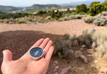 Compass in hand in mountains during Hiking. Tourist compass for orientation on terrain. Magnetic declination сalculator. Map reading and land navigation concept. Orient on maps in Spain mountains.