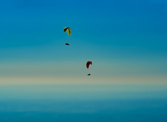 two paraglider sails soar through the air against a very blurred blue sky and sea to create a scene of enchantment