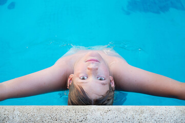 Close up horizontal photo of handsome boy looking up at camera. He is inside the pool in summer leaning on the edge with his arms outstretched. Enjoing vacations and relax lifestyle. Copy space.