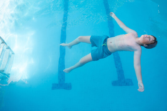 Horizontal photograph from above of Caucasian boy doing the dead in the pool floating relaxed with arms outstretched enjoying the peace and calmness on a sunny summer day. Copy space.