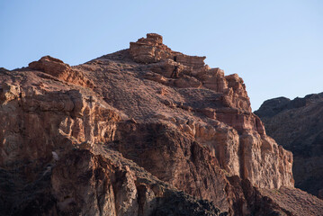 Fototapeta premium The rugged beauty of a desert landscape is captured as the sun casts its glow on sandstone spires, which stand proudly against a clear, pale sky.
