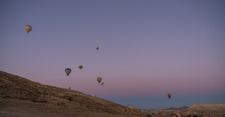 vibrant hot air balloons ascend into the tranquil sky, contrasting with the arid landscape below, creating a serene yet exhilarating spectacle at the cusp of day.