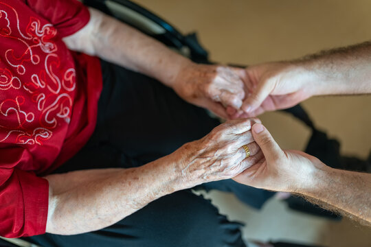 Hands of an elderly woman of high age holding the hands of a young man in an attitude of affection and accompaniment