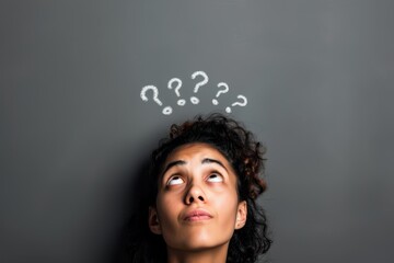 Young African American woman looking up at question marks drawn on a chalkboard, symbolizing curiosity and thinking.