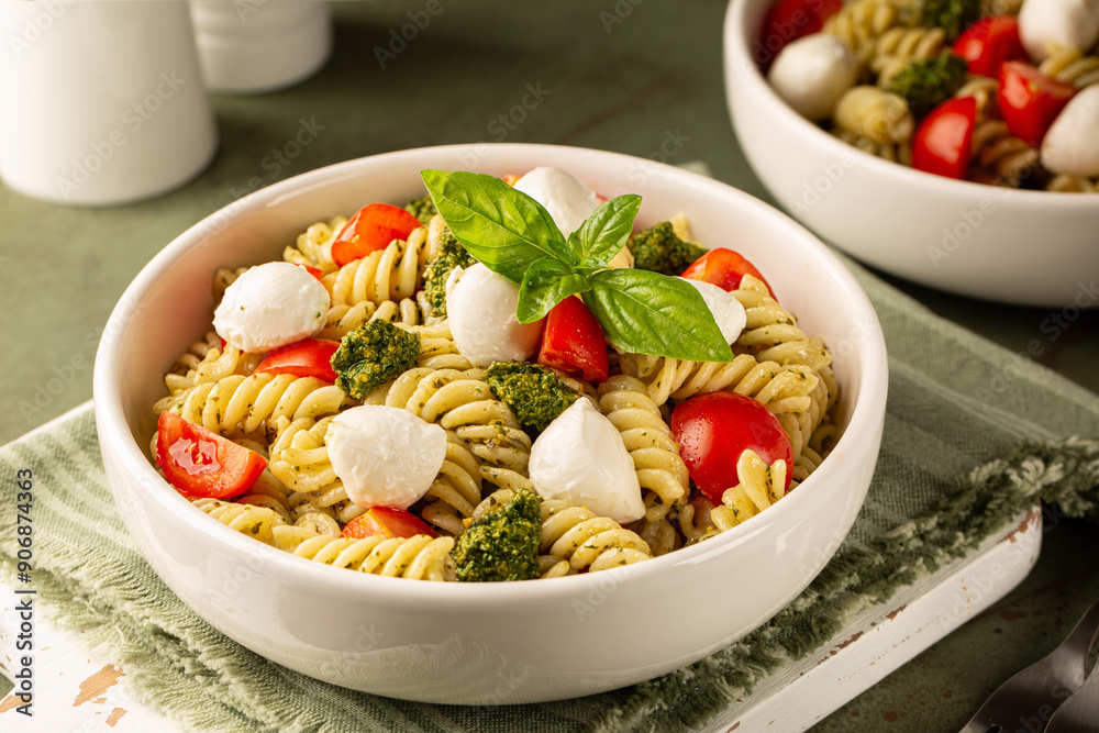 Poster Plate with cold pasta salad with homemade pesto sauce, tomato and mozzarella cheese, decorated with basil leaves on a green table surface. Italian lunch.