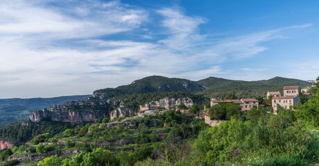 Verdant foliage frames the rugged beauty of stratified cliffs, with a backdrop of rolling hills extending into the horizon under a gentle sky.