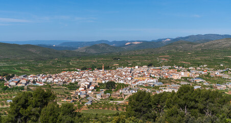 Naklejka premium panoramic view of a traditional Spanish town with clustered houses and a church spire, amid vast green landscapes and rolling hills under a clear sky.