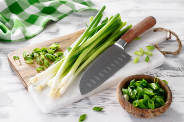 Marble cutting board with cut fresh green onions on wooden white table