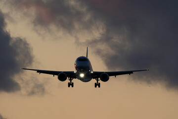 Airplane flying in the blue sky with clouds at sunset time.