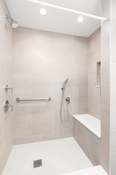 A brown tiled walk-in shower with a chrome faucet, bench seat, and square tiled floor.