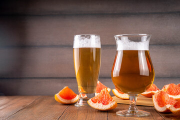 Glasses with Sour Grapefruit Craft Beer or Ale on wooden table with fresh pink grapefruit slices