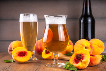 Glasses with Sour Sweet fruit Peach Craft Beer or Ale on wooden table with fresh peach slices
