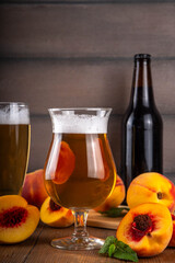 Glasses with Sour Sweet fruit Peach Craft Beer or Ale on wooden table with fresh peach slices
