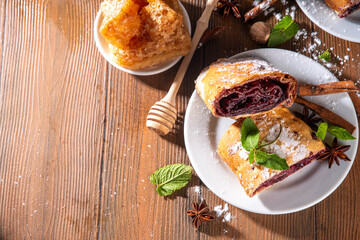 Homemade fragrant autumn cherry strudel with raisins, nuts, honey, cinnamon spices, on plate on kitchen table copy space 