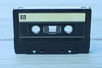 one old black retro magnetic tape and music recording in plastic transparent box audio cassette stands on gray wooden table