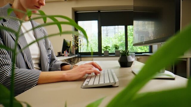 close-up female young hands typing and pressing a button on a white office device keyboard, nude manicure, professional keyboard through landscaping
