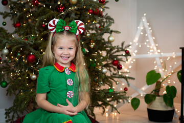 Portrait of a cute Caucasian little girl in Elf costume near the Christmas tree. Kids and Christmas concept