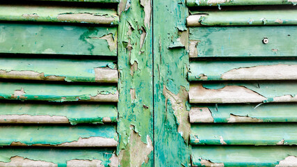 Close-up of weathered, peeling green paint on old wooden shutters symbolizing decay and the concept of abandonment
