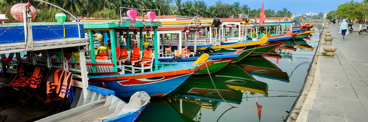 Vibrant, colorful lantern-decorated boats docked by the riverbank in Hoi An, Vietnam, highlighting Asian cultural heritage and tourism