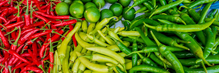 A colorful assortment of fresh, vibrant red, yellow, and green chili peppers and limes at a farmers market, ideal for Mexican cuisine and Cinco de Mayo celebrations