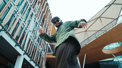 Low angle view of hipster pose in hip hop style surrounded by mall view. Portrait of sporty asian hip hop choreographer dancing break dance while looking at camera. Outdoor sport 2024. Hiphop.