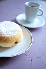 Close-up of berliner cake on a white plate and a cup of espresso