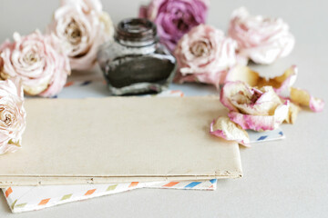 An old sheet of paper, pen, inkwell and many roses around it.