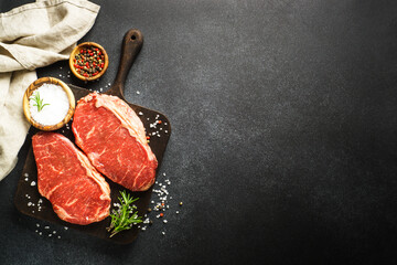 Raw beef meat with spices. Fresh meat steaks at black board. Top view.