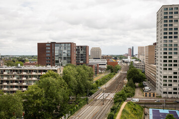 Fototapeta premium Spoorpark rail park and train track near rooftop view of Dutch city Tilburg in the Netherlands. Apartment blocks and skyrises next to train station in Holland under cloudy sky on grey day