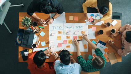 Top down aerial view of business team making scrum task board at meeting room. Group of people writing at paper and sticky notes for making kanban board to manage work flow. Top view. Convocation.