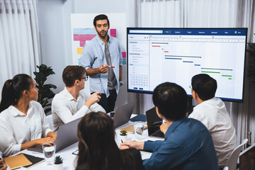 Project manager communicate and collaborate with team using project management software display on monitor, tracking progress of project task and making schedule plan at meeting table. Prudent