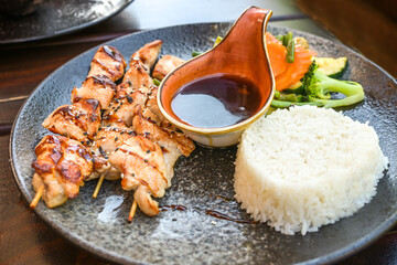 Chicken skewers, jasmine rice and vegetables with a spicy teriyaki sauce, Asian style food served on a dark plate, selected focus