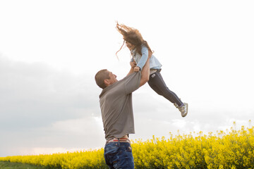 father playing with daughter throwing her up against sky background. walk in blooming field