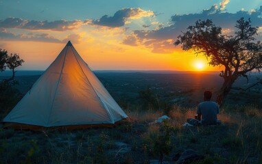 An adult Hispanic person sits peacefully watching the sunset beside a tent in a tranquil wilderness setting