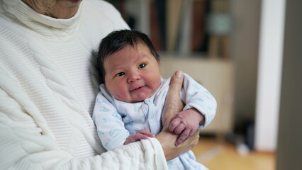 Close-up newborn baby held in arms by grandmother during first days of life, initial stages of...