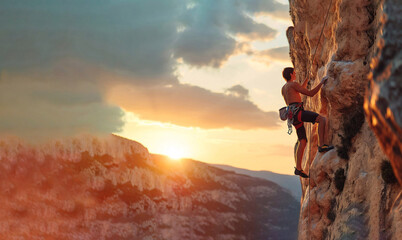 Young man climbing a rock against the backdrop of a beautiful su