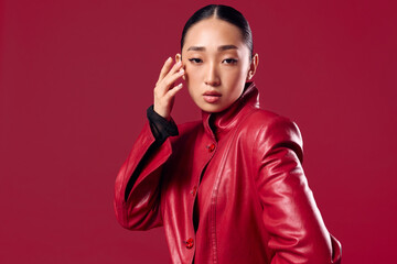 Fashion asian brunette in red leather jacket posing with eyes closed against red background