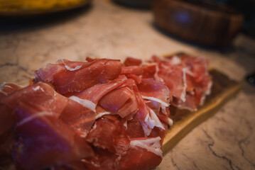 Elegant presentation of thinly sliced prosciutto on a wooden board, set against a marble countertop, highlighting the luxury and attention to detail in upscale dining.