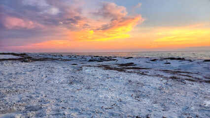 A beach scene during sunset or sunrise with the sky displaying a gradient of colors from blue to orange, reflecting on the water’s surface.