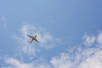 A passenger plane flies high in the blue sky with light clouds.