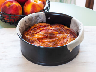 Vegan peach cake in baking mould on green table outdoors