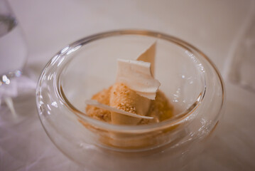 Sophisticated dessert in a clear glass bowl with white chocolate shards, set on a white tablecloth with a glass of water, showcasing luxury hotel dining.