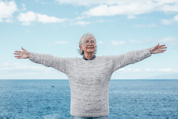 Happy senior woman standing by the sea with outstretched arms. Smiling elderly lady in outdoor...