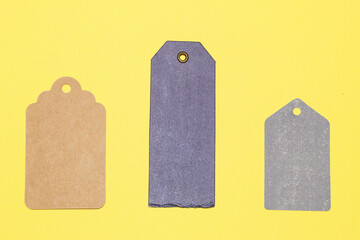 Three blank cardboard labels of different sizes, colors and shapes on a yellow background. Price tags.