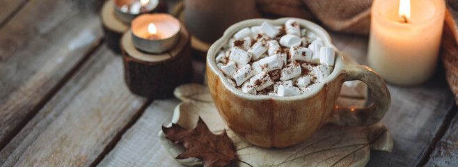 Spicy sweet fall hot drink: delicious pumpkin latte with cinnamon, marshmallow with salted caramel. Served in handmade artisan mug in shape of pumpkins, cozy home decor with candles, dry autumn leaves