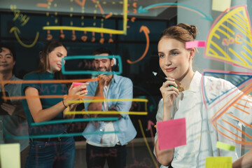 Young beautiful businesswoman writing business plan to investor on glass wall. Skilled female leader presenting marketing strategy by using graph. Smart manager presenting marketing idea. Tracery.