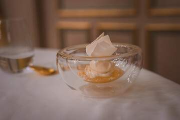 A sophisticated dessert of meringue and creamy mousse atop fruit compote, served in a double-walled glass bowl on a white tablecloth in a high-end European hotel.