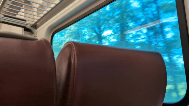 view of row of seats and window on moving train (blurry trees passing by quickly outside) railroad transport travel riding metro subway rural tourism
